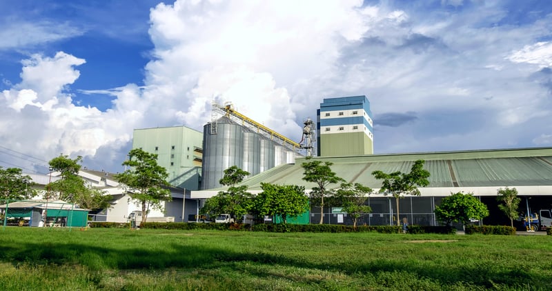 Large factory surrounded by green trees and grass field