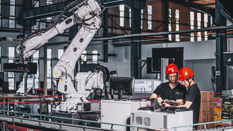 Two men working in a factory controlling a robot